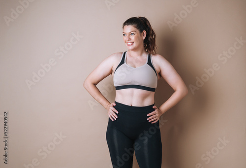 Self loving young woman plus size in sport wear on beige background, body love