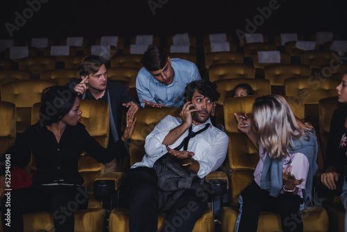 Caucasian white young woman admonish young man for using cellphones in cinema.