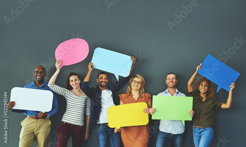 Smiling casual team of diverse people holding opinion speech bubbles, to voice their important communication message. Creative group standing with colorful copyspace sign boards together in a row photo