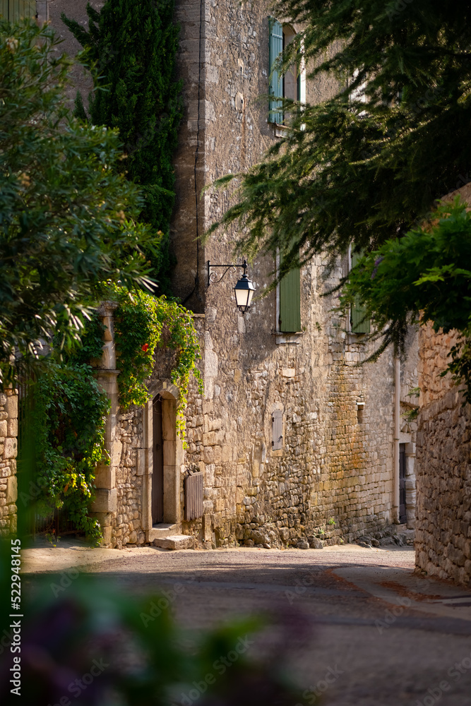 Narrow street in Montclus sur Cèze in Provence, southern France. Sunset atmosphere with warm evening light, street lantern, old town facades and vegetation. Idyllic and romantic street view in summer.