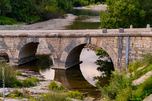 Old bridge spanning over Cèze river in Provence south France near idyllic village Montclus. Evening atmosphere with brick arches reflected on water surface. Very low water level caused by drought.