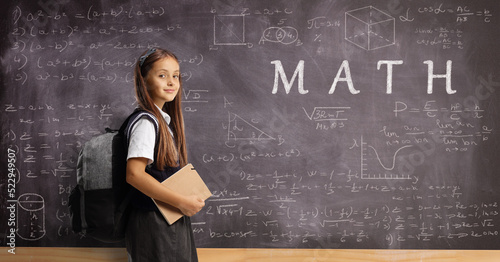 Schoolgirl with a backpack and book in front of a blackboard with numbers and math