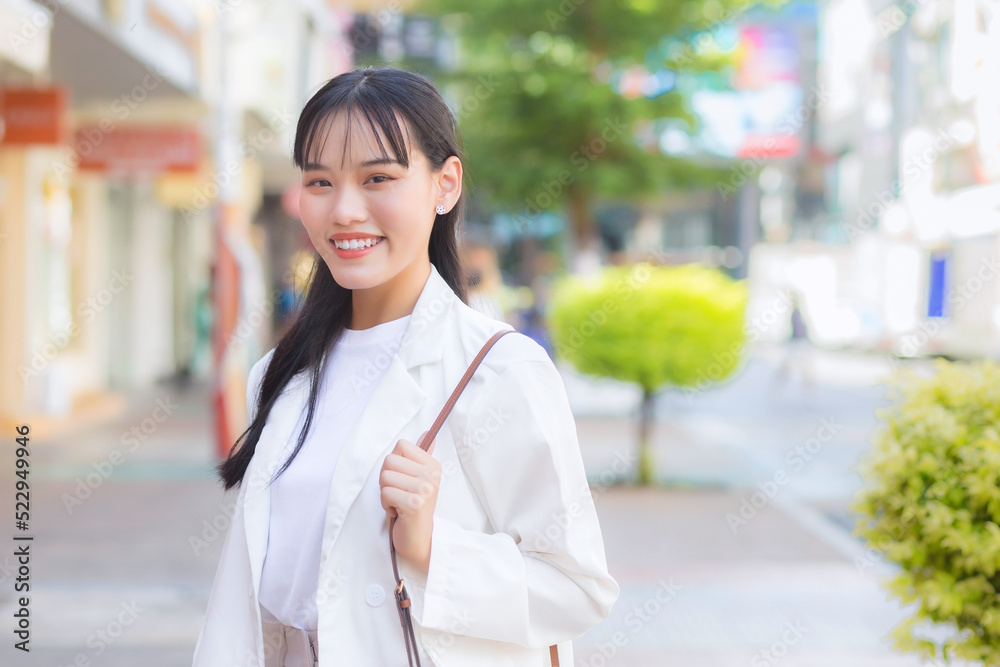 Confident young business Asian working woman who wears a white shirt and shoulder bag smiles happily while she is walking to work at office in the city. Confident young business Asian working woman who wears a white shirt and shoulder bag smiles happily while she is walking to work at office in the city.