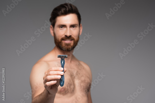 blurred and shirtless man with beard holding safety razor isolated on grey.