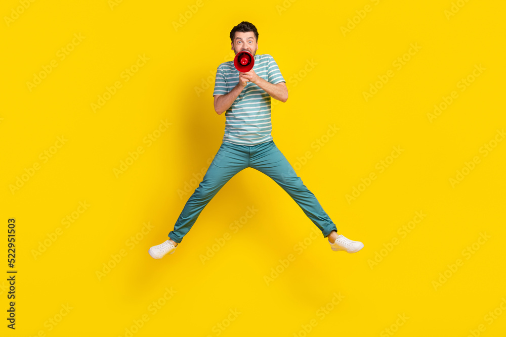 Full length photo of crazy man student dressed striped t-shirt blue trousers screaming in loudspeaker isolated on yellow color background
