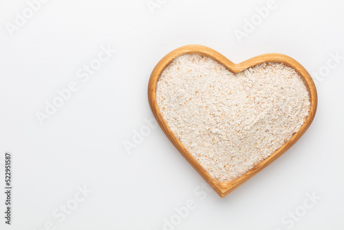 Wheat flour in a wooden heart shape bowl on a pastel background.