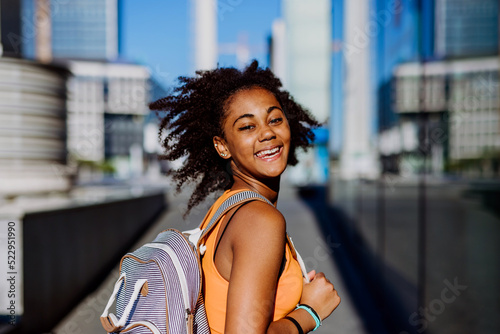 Multiracial teenage girl walking with backpack in modern city centre during summer day, back to school concept. © Halfpoint
