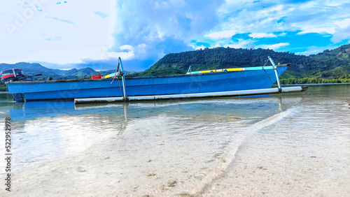 long boat made of blue fiber.  he was parked on the edge of a fine white sandy beach with clear sea water at Ratu Beach, Boalemo Regency, Gorontalo Province.  Outdoor photo taken on August 11, 2022 photo