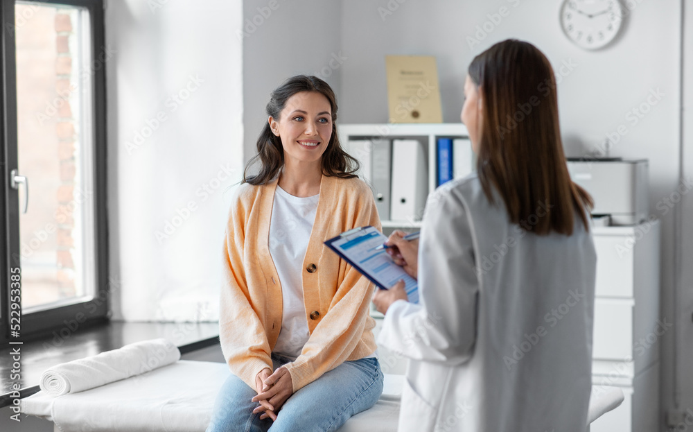 medicine, healthcare and people concept - female doctor with clipboard talking to smiling woman patient at hospital - obrazy, fototapety, plakaty 