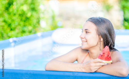 Smiling teen girl eats watermelon in the pool at sunny day. Empty space for text