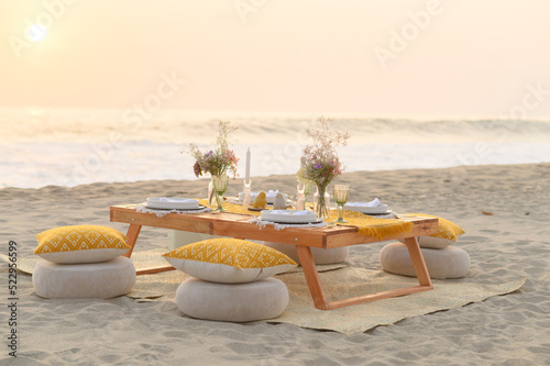 Small wooden decorated table placed on sandy seashore before romantic dinner photo