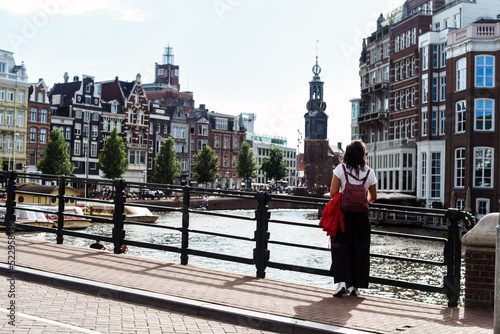 Mujer joven parada en un puente de la ciudad de Ámsterdam. Vistas de edificios tradicionales holandeses