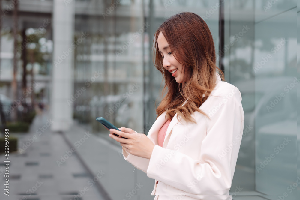 Beautiful asian female businesswoman use smartphone, Walk enjoy smiling while doing commuting in the modern city near office building outside. Beautiful asian female businesswoman use smartphone, Walk enjoy smiling while doing commuting in the modern city near office building outside.