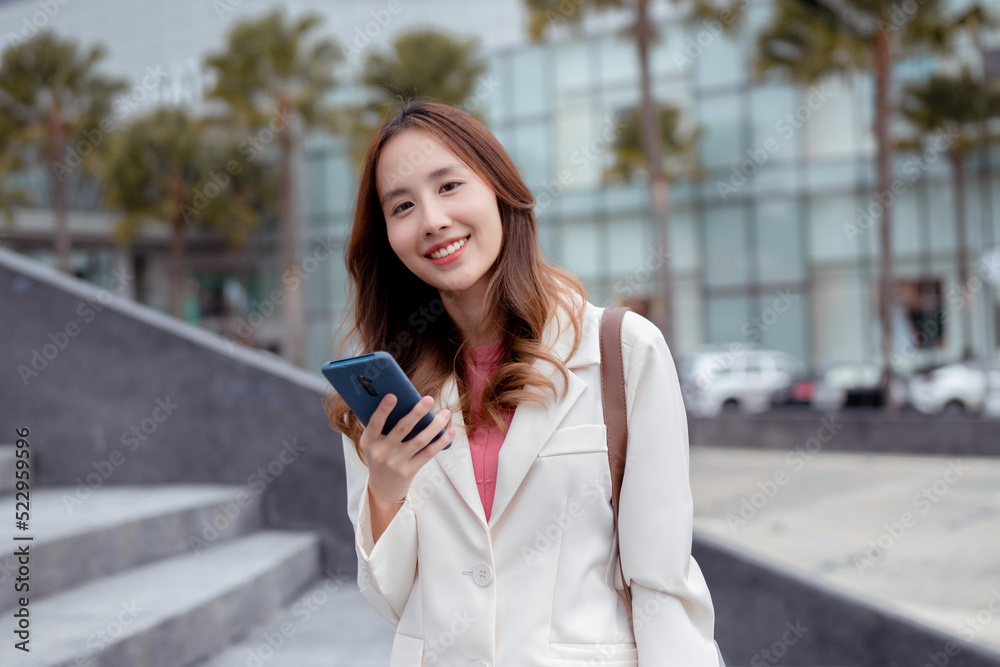Beautiful asian female businesswoman use smartphone hold paper cup of hot drink, Walk enjoy smiling while doing commuting in the modern city near office building outside Beautiful asian female businesswoman use smartphone hold paper cup of hot drink, Walk enjoy smiling while doing commuting in the modern city near office building outside