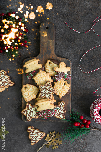 Different shape Christmas cookies on wooden cut board with Christmas decoration. Festive homemade treat .Top view