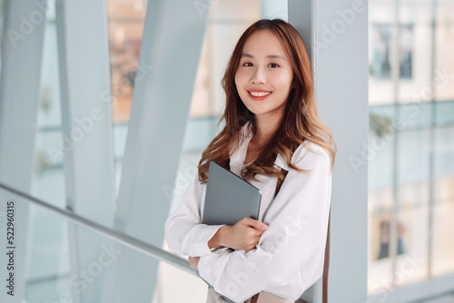 Beautiful asian female businesswoman hold laptop computer, Smart woman enjoy smiling while doing commuting in office workplace
