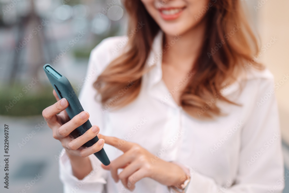 Closeup Smiling of asian female businesswoman use smartphone, Walk enjoy smiling while doing commuting in the modern city near office building outside Closeup Smiling of asian female businesswoman use smartphone, Walk enjoy smiling while doing commuting in the modern city near office building outside