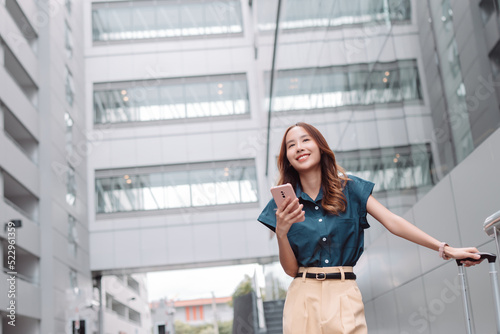 Beautiful asian female businesswoman use smartphone, Walk enjoy smiling while doing commuting in the modern city near office building outside