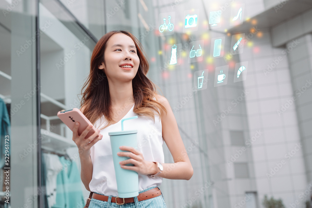 Smiling asian businesswoman use smartphone and hold reusable eco-friendly ecological cup outside shopping mall store while commuting in city, Futuristics online shopping innovation concept Smiling asian businesswoman use smartphone and hold reusable eco-friendly ecological cup outside shopping mall store while commuting in city, Futuristics online shopping innovation concept