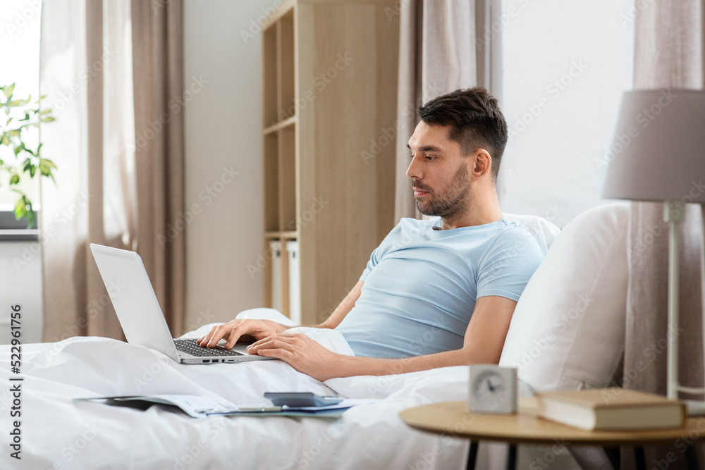 people, technology and remote job concept - man with laptop computer lying in bed at home bedroom people, technology and remote job concept - man with laptop computer lying in bed at home bedroom