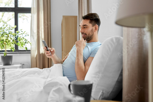 technology, internet and people concept - smiling man texting on smartphone in bed at home in morning © Syda Productions