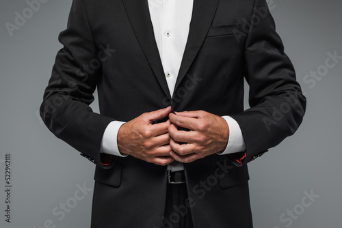cropped view of elegant man in black tuxedo adjusting blazer isolated on grey.