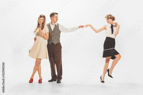 Portrait of stylish man in retro suit flirting with two beautiful women isolated over white studio background