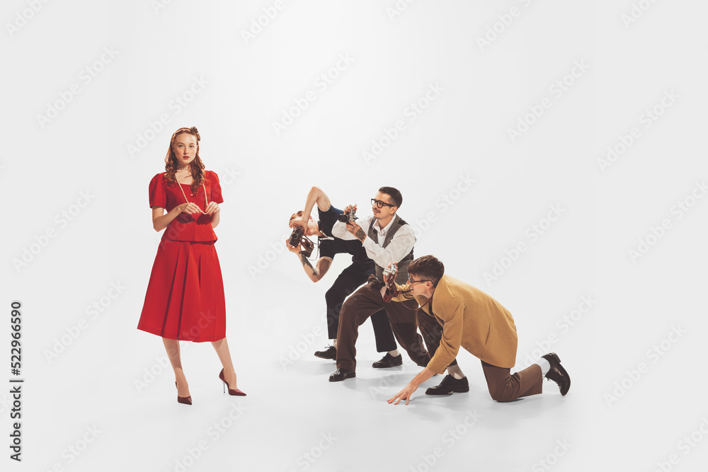Group of young men in stylish suits taking photo of beautiful woman in red dress isolated over white studio background. Popularity Group of young men in stylish suits taking photo of beautiful woman in red dress isolated over white studio background. Popularity