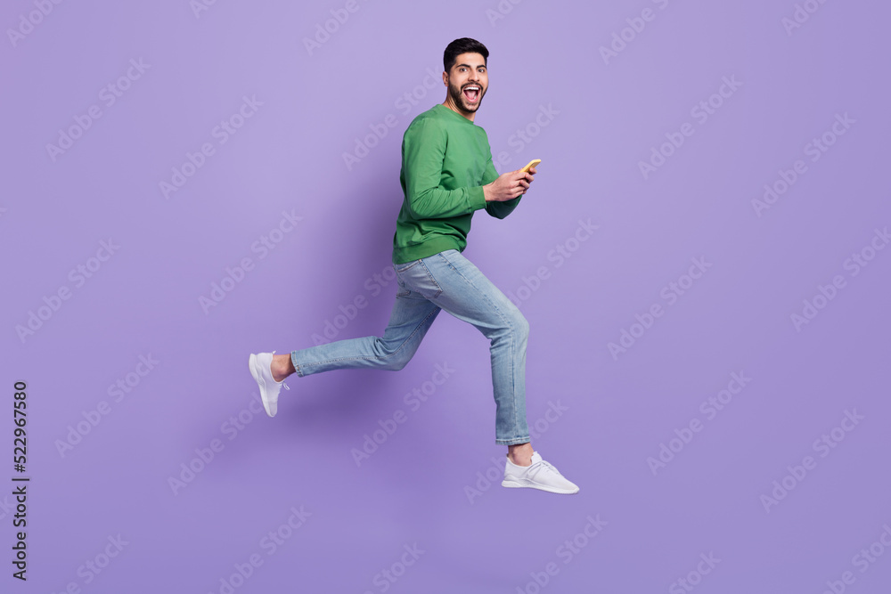 Full body photo of young latin guy hold device impressed repost like jumping wear stylish green clothes isolated on purple color background