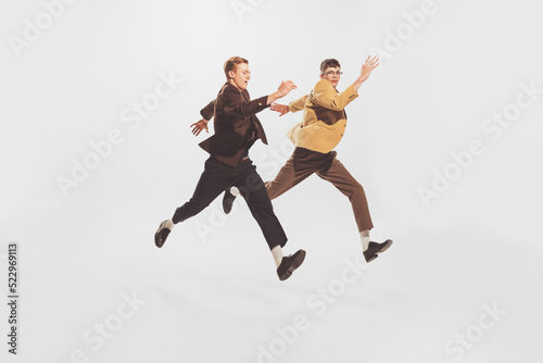 Portrait of two stylish men, friends spending time together, posing in a jump isolated over white studio background
