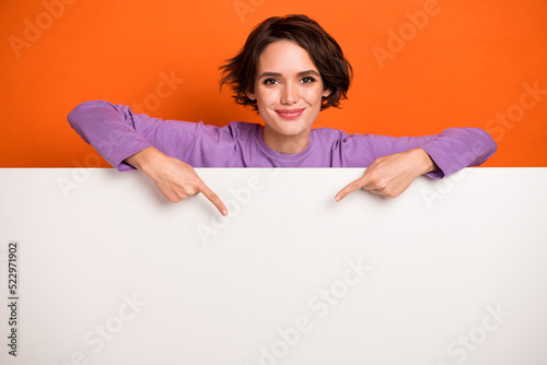 Photo of funky shiny girl dressed purple pullover pointing white placard empty space isolated orange color background