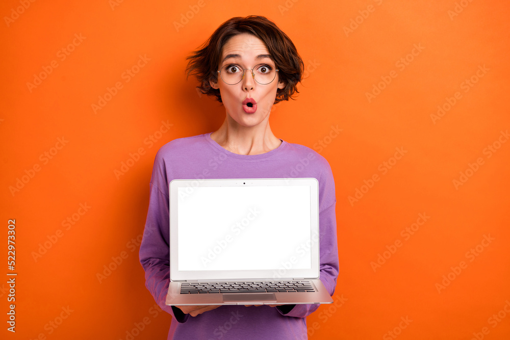 Photo of excited shiny lady wear violet sweatshirt spectacles showing modern device empty space isolated orange color background Photo of excited shiny lady wear violet sweatshirt spectacles showing modern device empty space isolated orange color background
