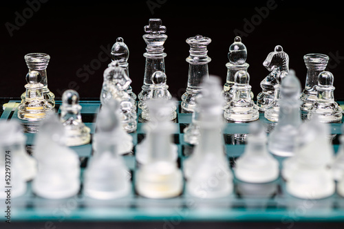 glass, transparent chess pieces on a checkerboard, selective focus, close-up, isolated on black