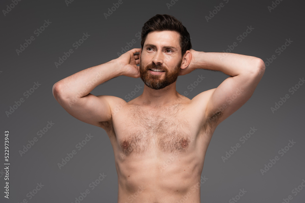 Fototapeta premium shirtless and happy man with hair on chest posing with hands behind head isolated on grey.