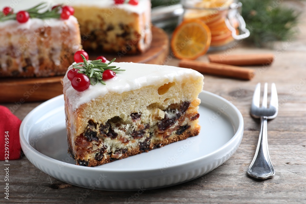 Slice of traditional Christmas cake decorated with rosemary and cranberries on wooden table, closeup Slice of traditional Christmas cake decorated with rosemary and cranberries on wooden table, closeup