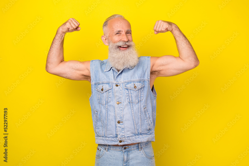 Photo of strong cool retired guy wear jeans waistcoat smiling rising fists showing arm muscles isolated yellow color background Photo of strong cool retired guy wear jeans waistcoat smiling rising fists showing arm muscles isolated yellow color background
