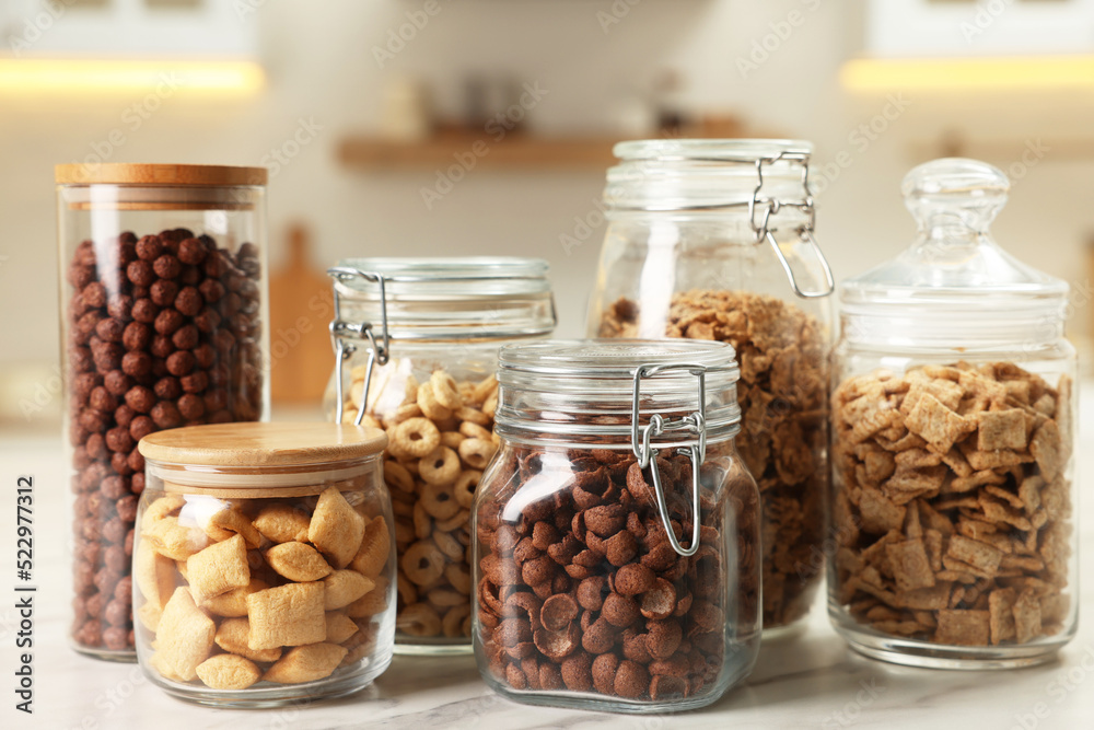 Glass containers with different breakfast cereals on white marble table in kitchen Glass containers with different breakfast cereals on white marble table in kitchen