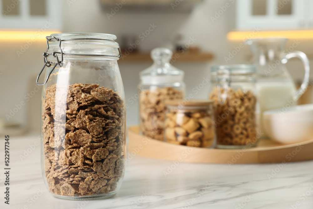 Glass container with bran flakes on white marble table in kitchen. Space for text Glass container with bran flakes on white marble table in kitchen. Space for text
