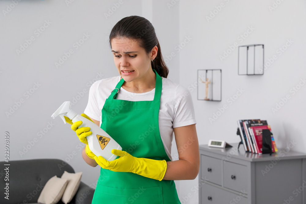 Woman looking at bottle of toxic household chemical with warning sign indoors Woman looking at bottle of toxic household chemical with warning sign indoors