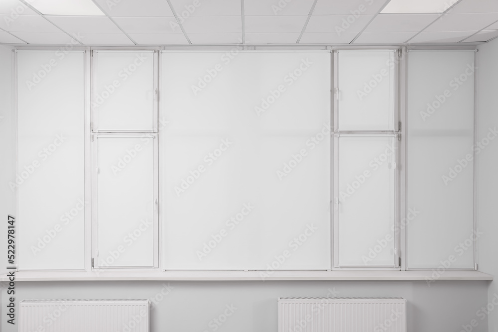 Windows covered with white roller blinds indoors Windows covered with white roller blinds indoors