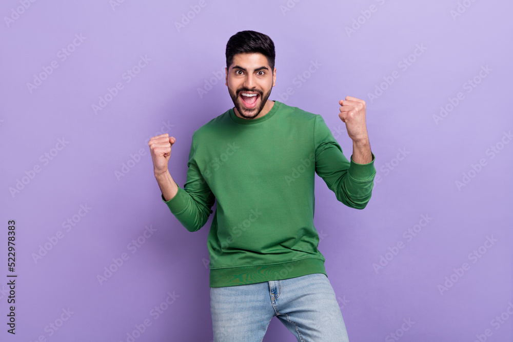 Photo portrait of yelling young hispanic man raise fists support favorite team wear trendy green outfit isolated on violet color background Photo portrait of yelling young hispanic man raise fists support favorite team wear trendy green outfit isolated on violet color background