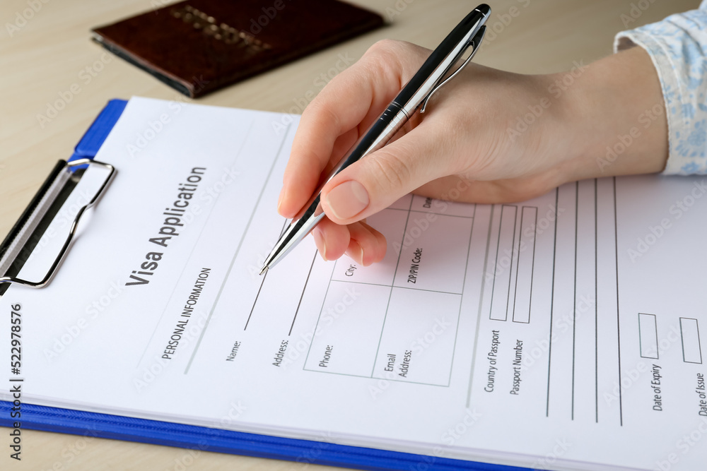 Woman filling visa application form for immigration at table, closeup Woman filling visa application form for immigration at table, closeup