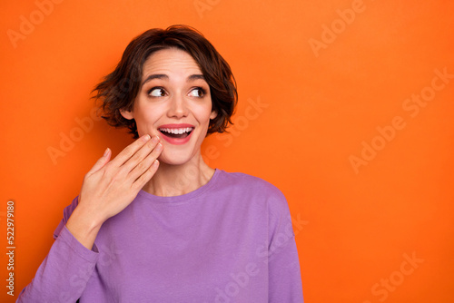 Photo of impressed cheerful girl hand near mouth look interested empty space isolated on orange color background © deagreez