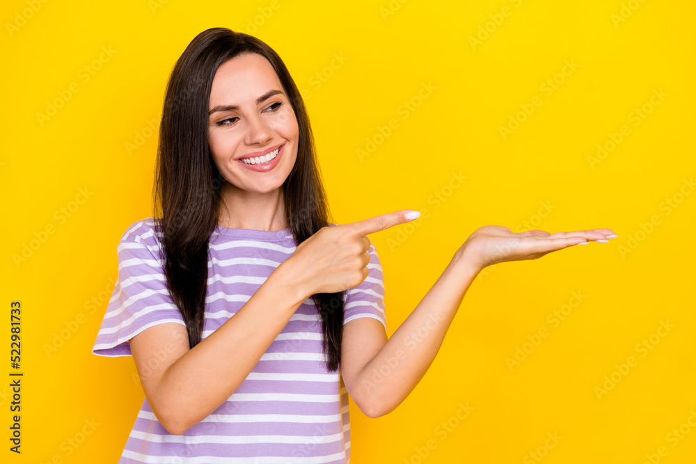 Photo of young smiling cute toothy girl showing object looking interested arm empty space isolated on yellow color background Photo of young smiling cute toothy girl showing object looking interested arm empty space isolated on yellow color background