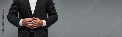 cropped view of elegant man in black tuxedo adjusting blazer isolated on grey, banner.