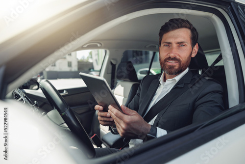 Handsome businessman working on digital tablet while sitting on driver seat in luxury car © Kostiantyn