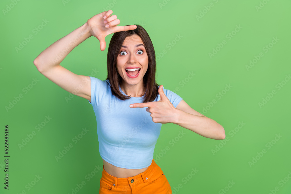 Portrait of cheerful overjoyed funky lady arms fingers demonstrate cadre gesture isolated on green color background Portrait of cheerful overjoyed funky lady arms fingers demonstrate cadre gesture isolated on green color background