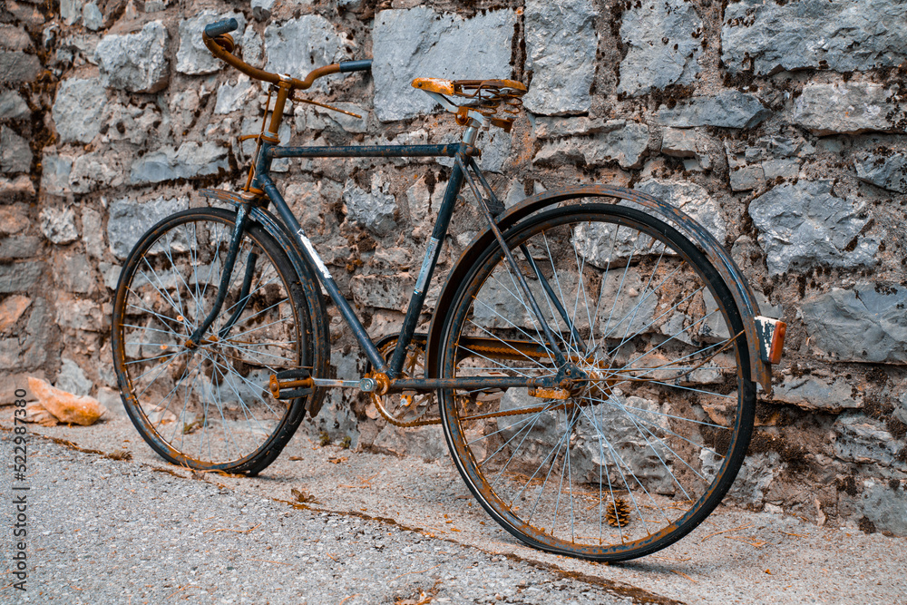 An old rusty two-wheeled bicycle stands against the background of a stone wall, ancient means of transportation.