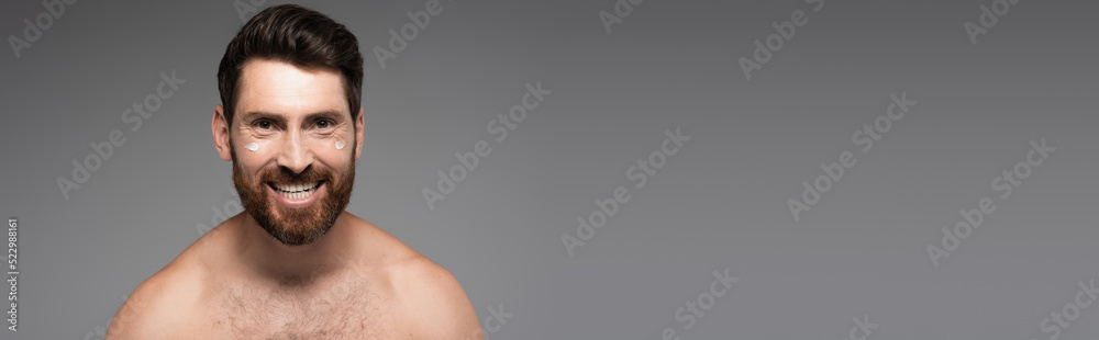 cheerful and bearded man with cream on face smiling isolated on grey, banner. cheerful and bearded man with cream on face smiling isolated on grey, banner.