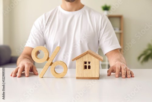 Bilde på lerret Cropped shot of young man sitting at white table with little wooden toy house model and percent sign